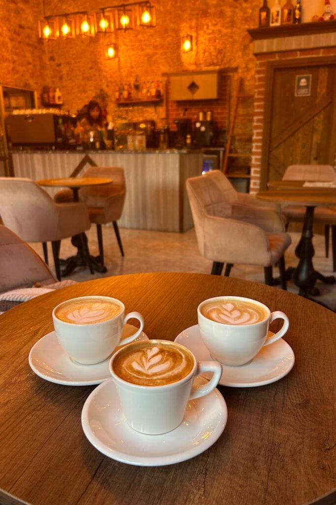 Warm-lit café in Türkiye with three cappuccinos on a wooden table.